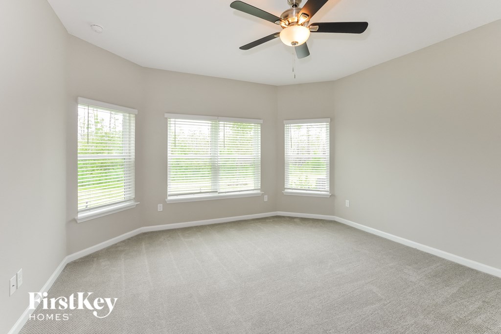 an empty room with a ceiling fan and three windows