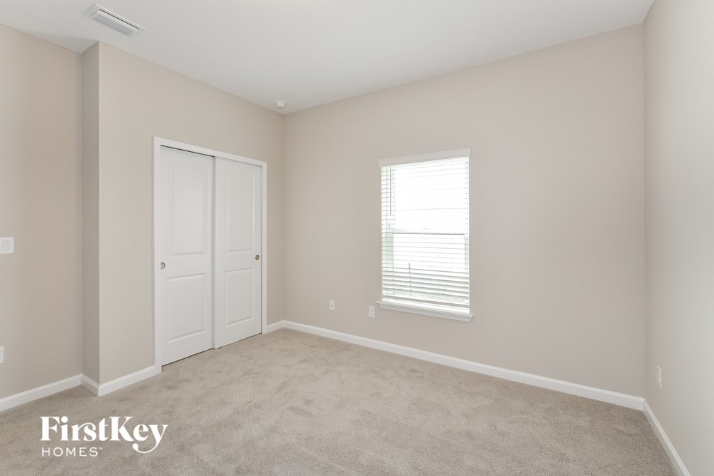 a bedroom with beige carpet and white doors and a window