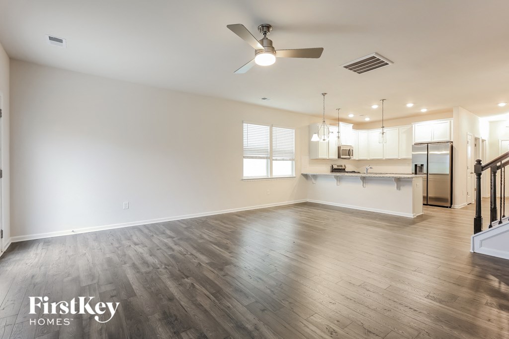 an empty living room and kitchen with wood floors and a ceiling fan