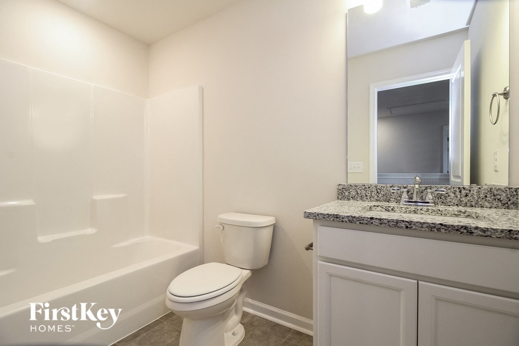 A white toilet sits in a bathroom with a granite counter and a mirror.