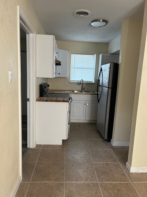 A kitchen with a refrigerator, sink, and cabinets.