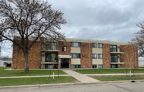 a brick apartment building with a sidewalk and a tree