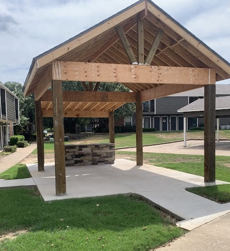 A wooden pavilion with a sloped roof and a concrete walkway in front.