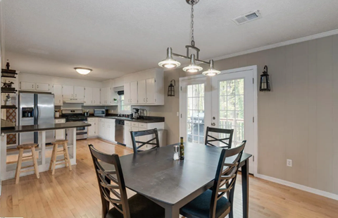 A kitchen with a table and chairs in the foreground and a refrigerator, oven, and cabinets in the background.