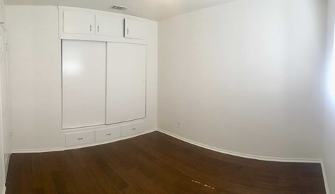 A white cabinet with two doors is in the corner of a room with wood flooring.