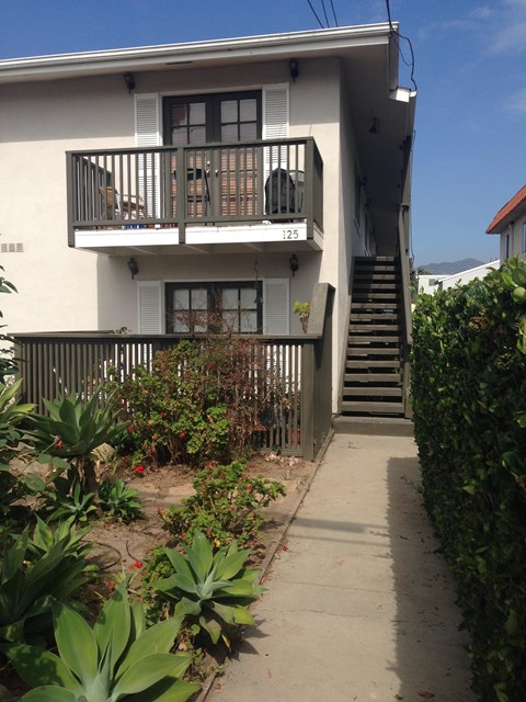 A white two-story building with a balcony and stairs leading up to it.