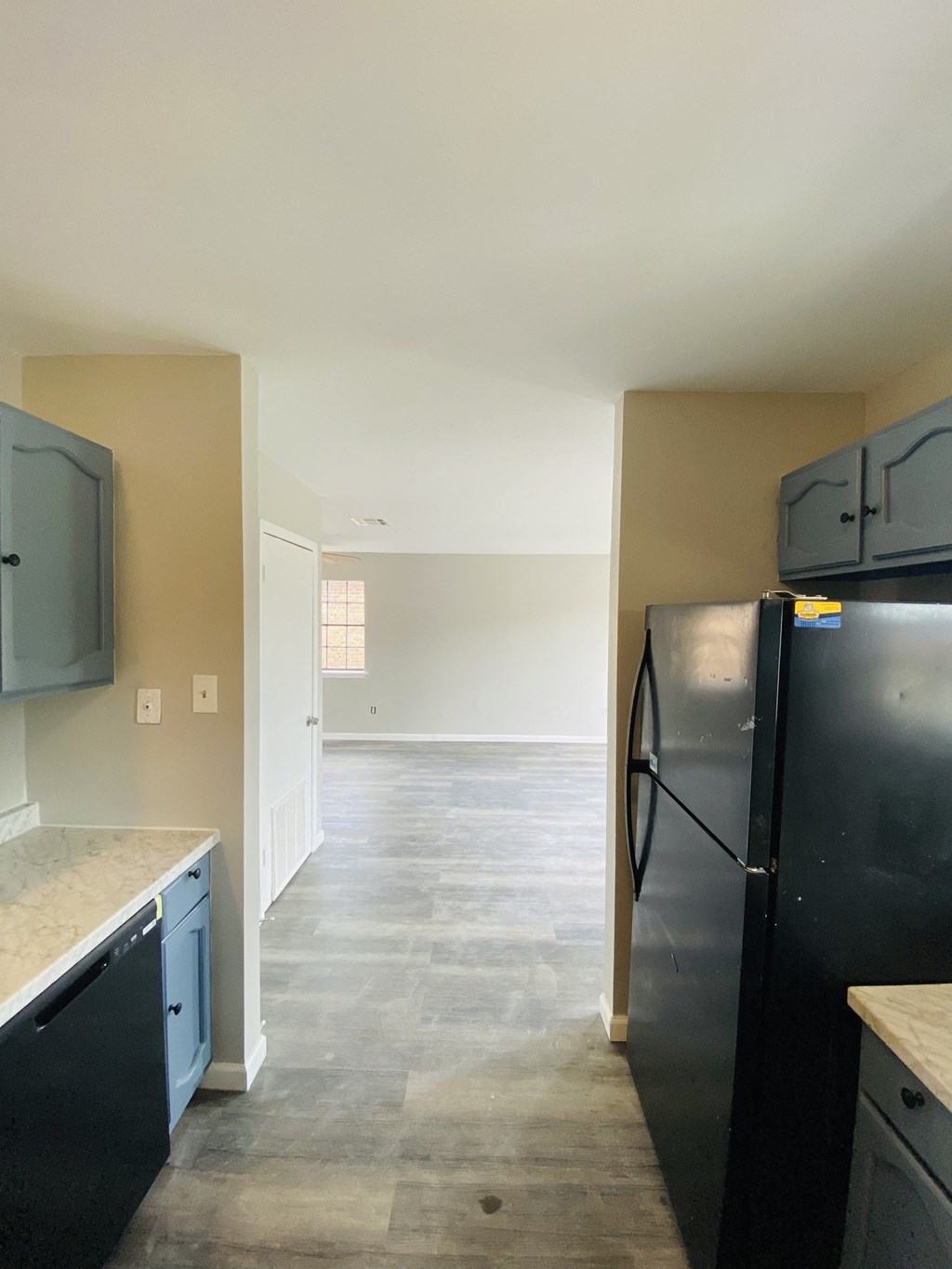 an empty kitchen with black appliances and a hallway to the living room