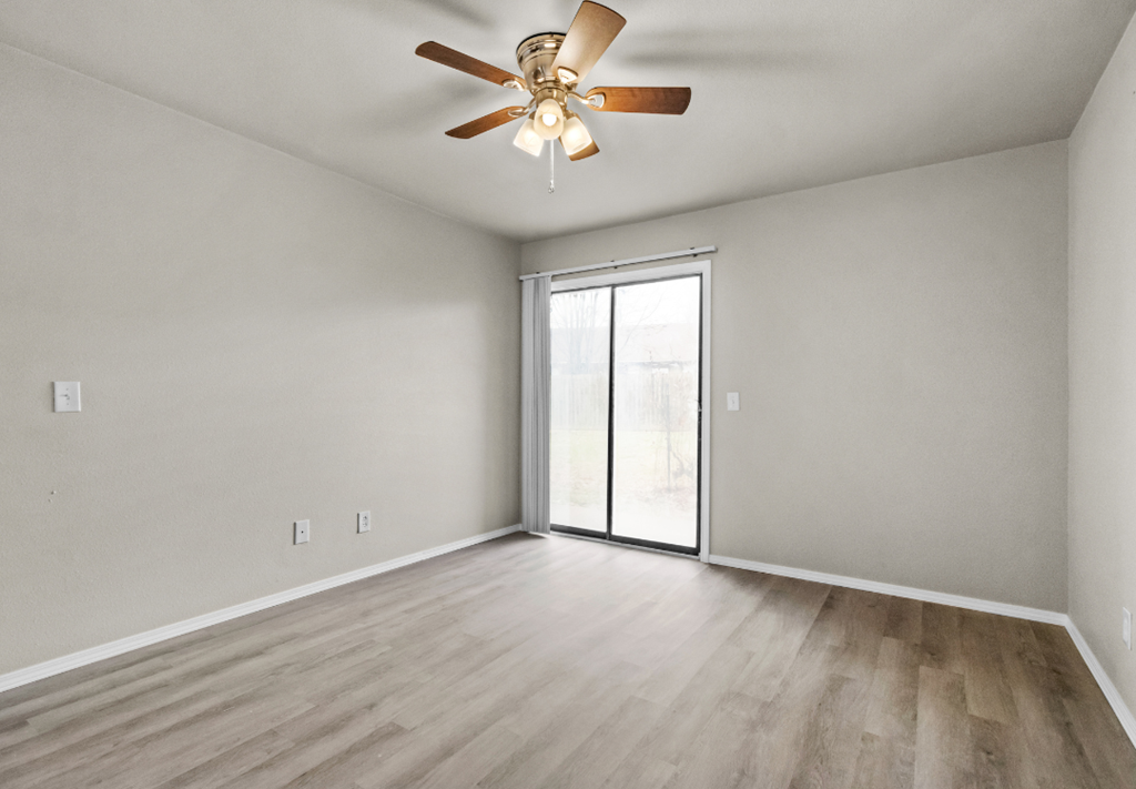an empty living room with a ceiling fan and a sliding glass door