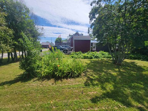 A red building is surrounded by greenery and a car is parked in the driveway.