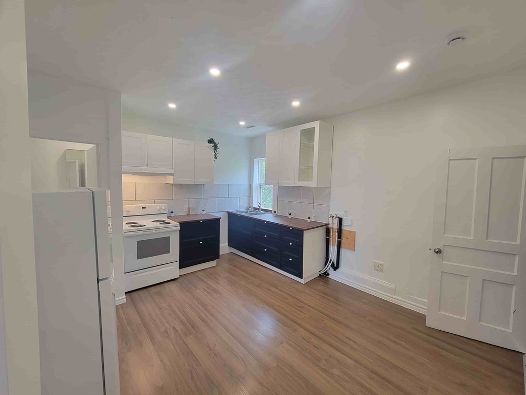 A kitchen with a white fridge, black dishwasher and wooden floors.