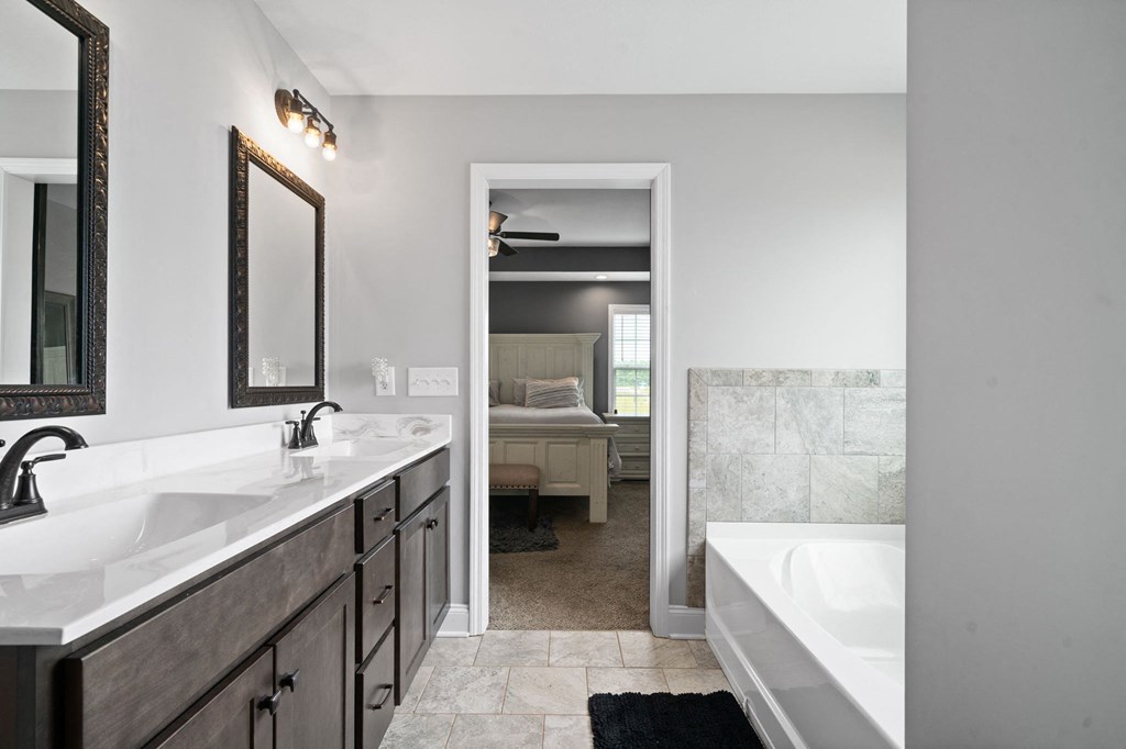 a bathroom with two sinks and a tub and a bedroom in the background