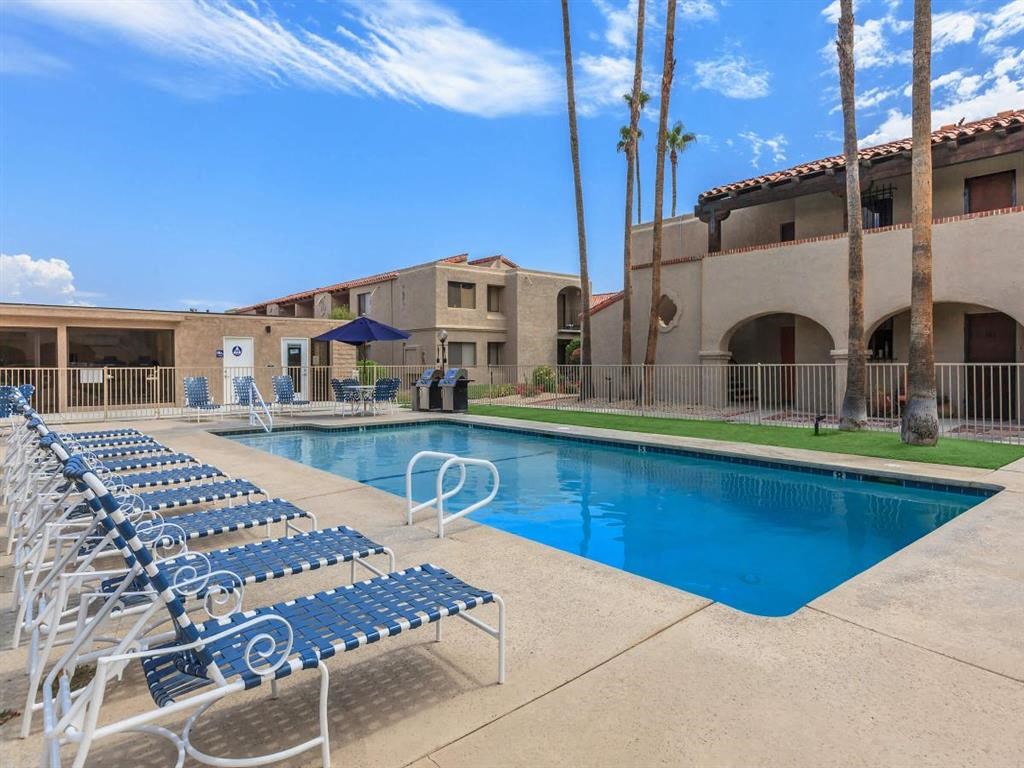 a swimming pool with blue chairs and a building in the background