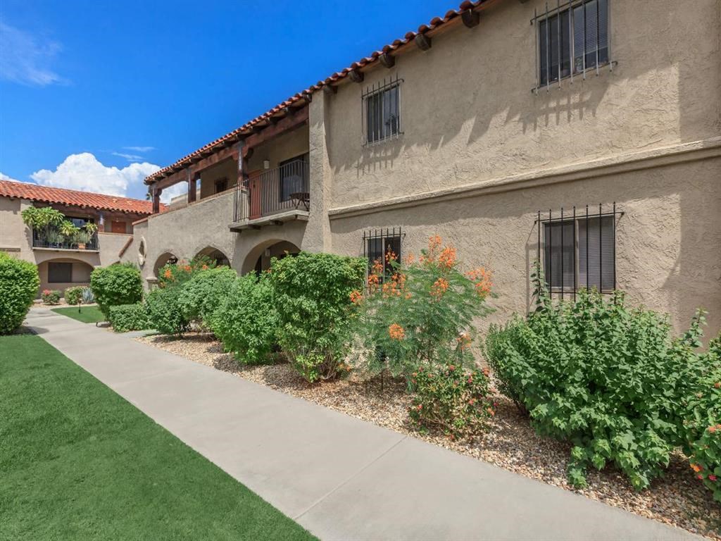 a sidewalk in front of a building with bushes and plants