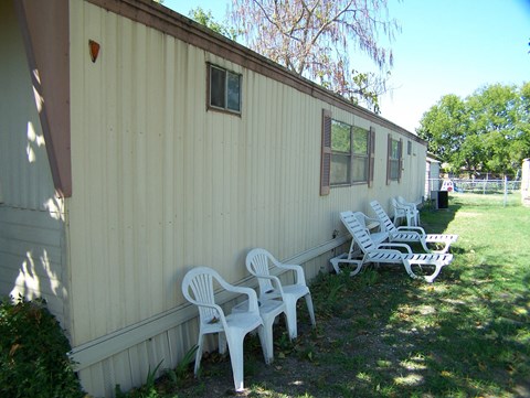 A row of white plastic chairs are lined up on a lawn in front of a tan building.