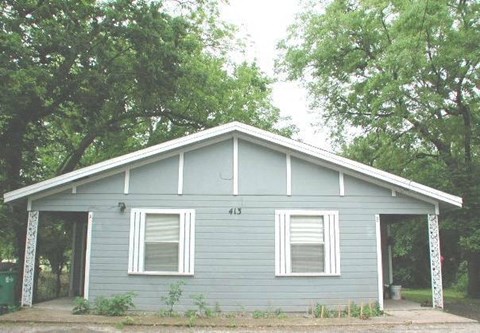 A small house with a grey siding and a white window is surrounded by trees.
