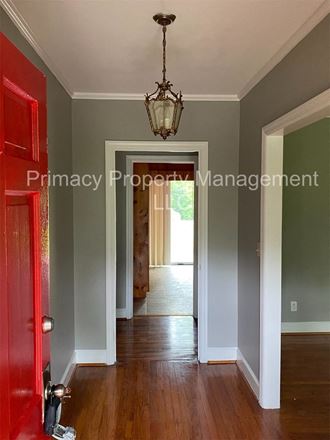 the hallway of a home with a red door and a chandelier