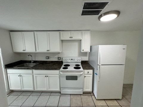 A white kitchen with a black counter top and white appliances.