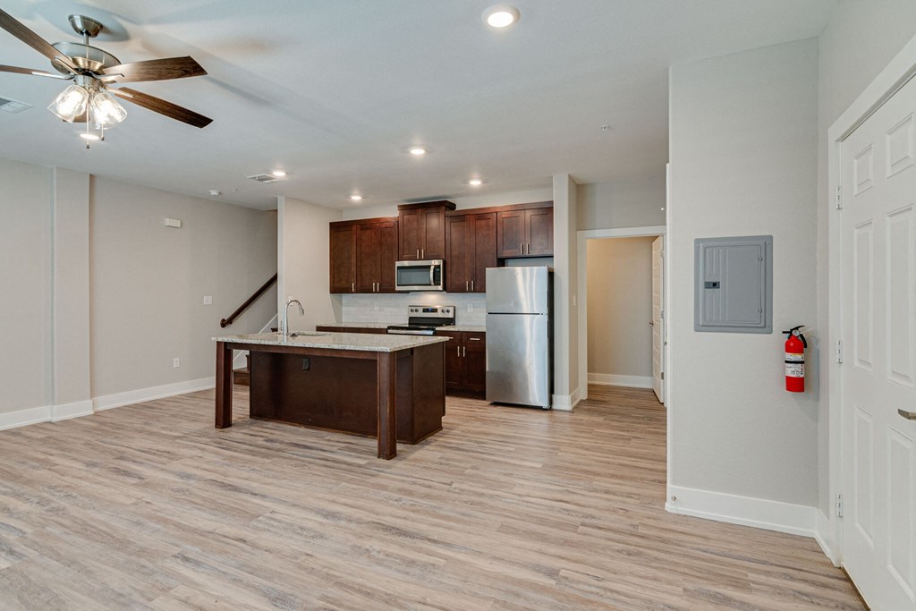 an empty living room with a kitchen and a ceiling fan