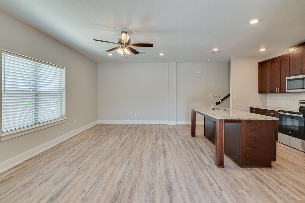 an empty living room with a kitchen and a ceiling fan