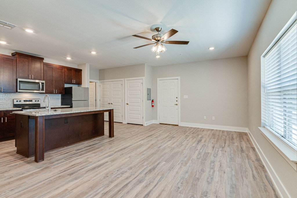 an empty living room with a kitchen and a ceiling fan
