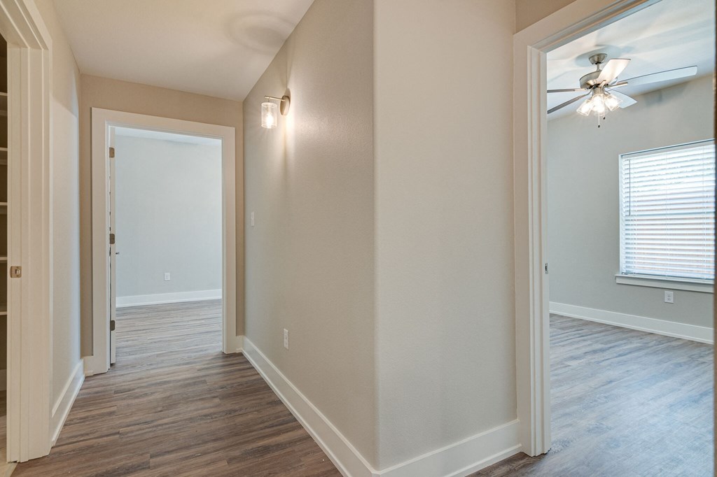 an empty living room with a ceiling fan and a door to a hallway