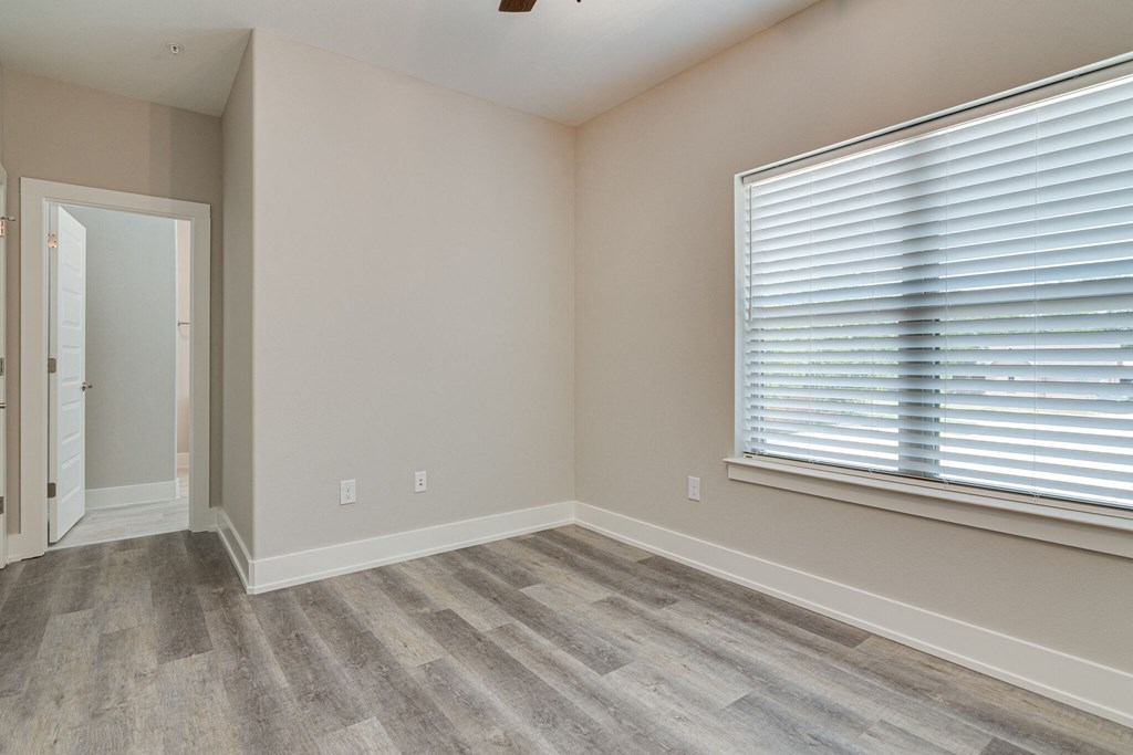 an empty bedroom with a large window and wood flooring
