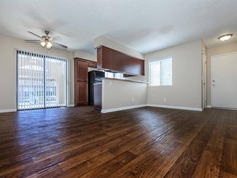 an empty living room with a kitchen and a ceiling fan