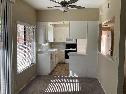 a white kitchen with a ceiling fan and a window