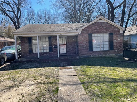 A small brick house with a porch and a car parked in front.