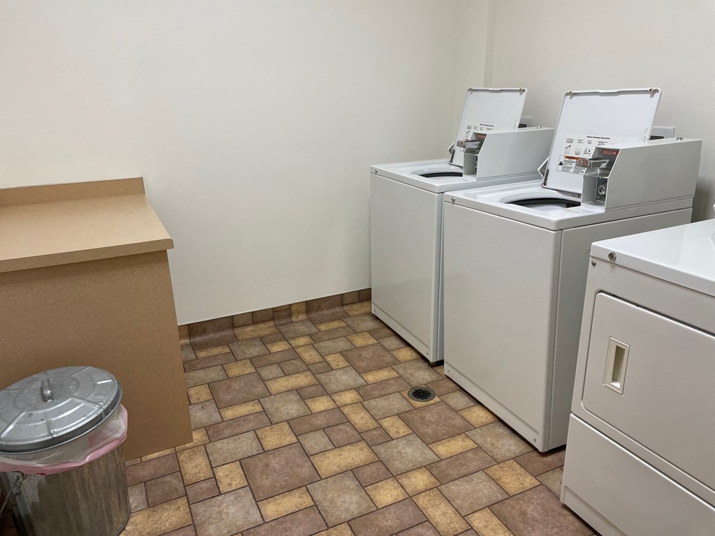 a laundry room with four washing machines and a trash can