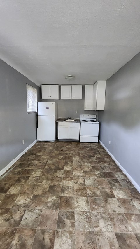 A kitchen with white appliances and brown tiled floors.
