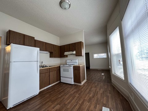 an empty kitchen with white appliances and wooden floors