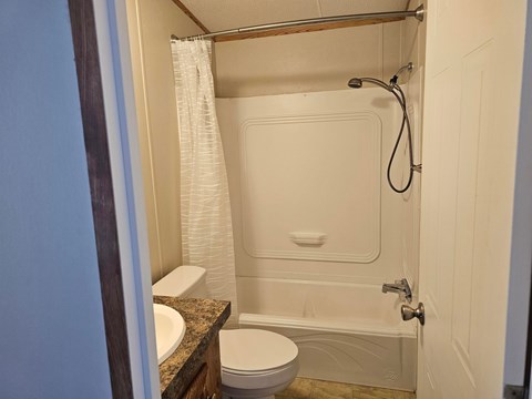 A white toilet sits next to a white bathtub in a small bathroom.