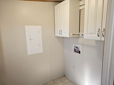 A white kitchen cabinet with a fridge and a white switchboard on the wall.