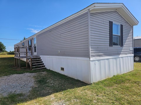 A mobile home with a deck and a car parked in the background.
