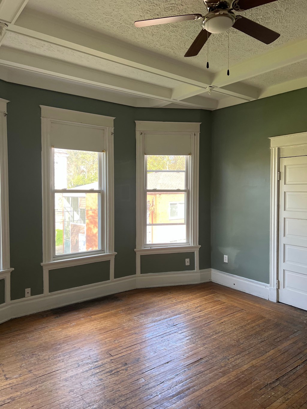 A room with a ceiling fan and two windows.