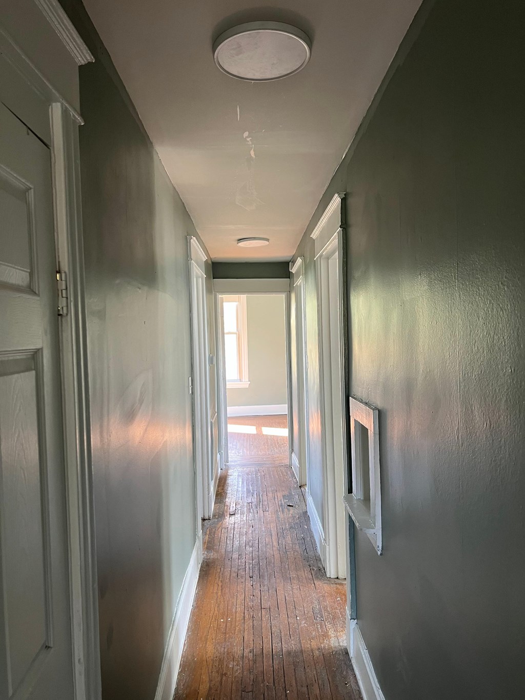 A long hallway with doors on the left and a light at the end.
