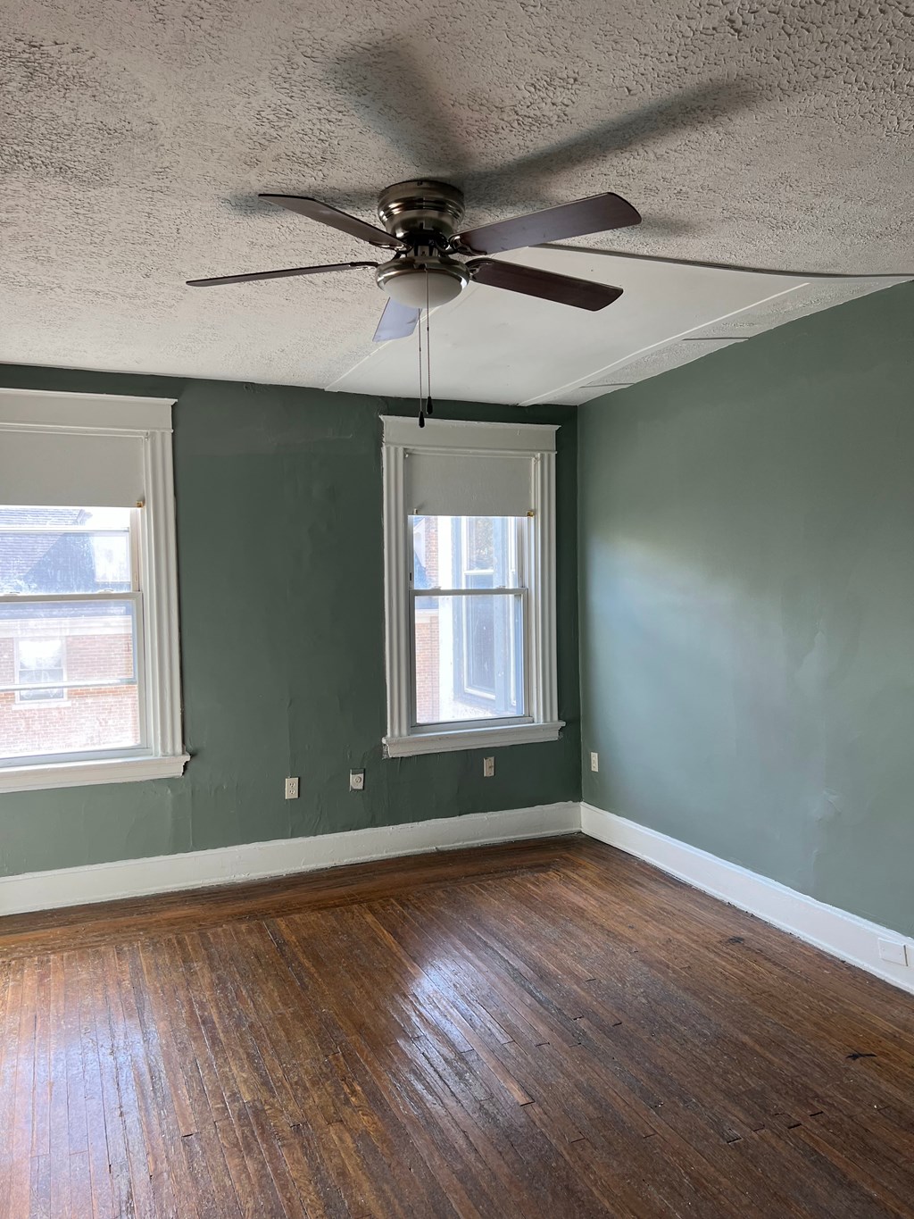 A room with a ceiling fan and two windows.