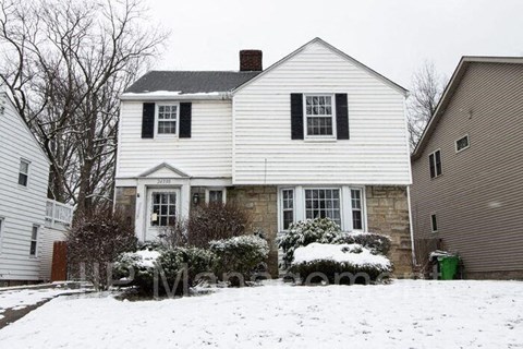 A white house with a black roof and a snow-covered front yard.