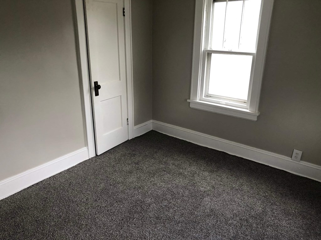 a room with gray carpet and a white door and a window