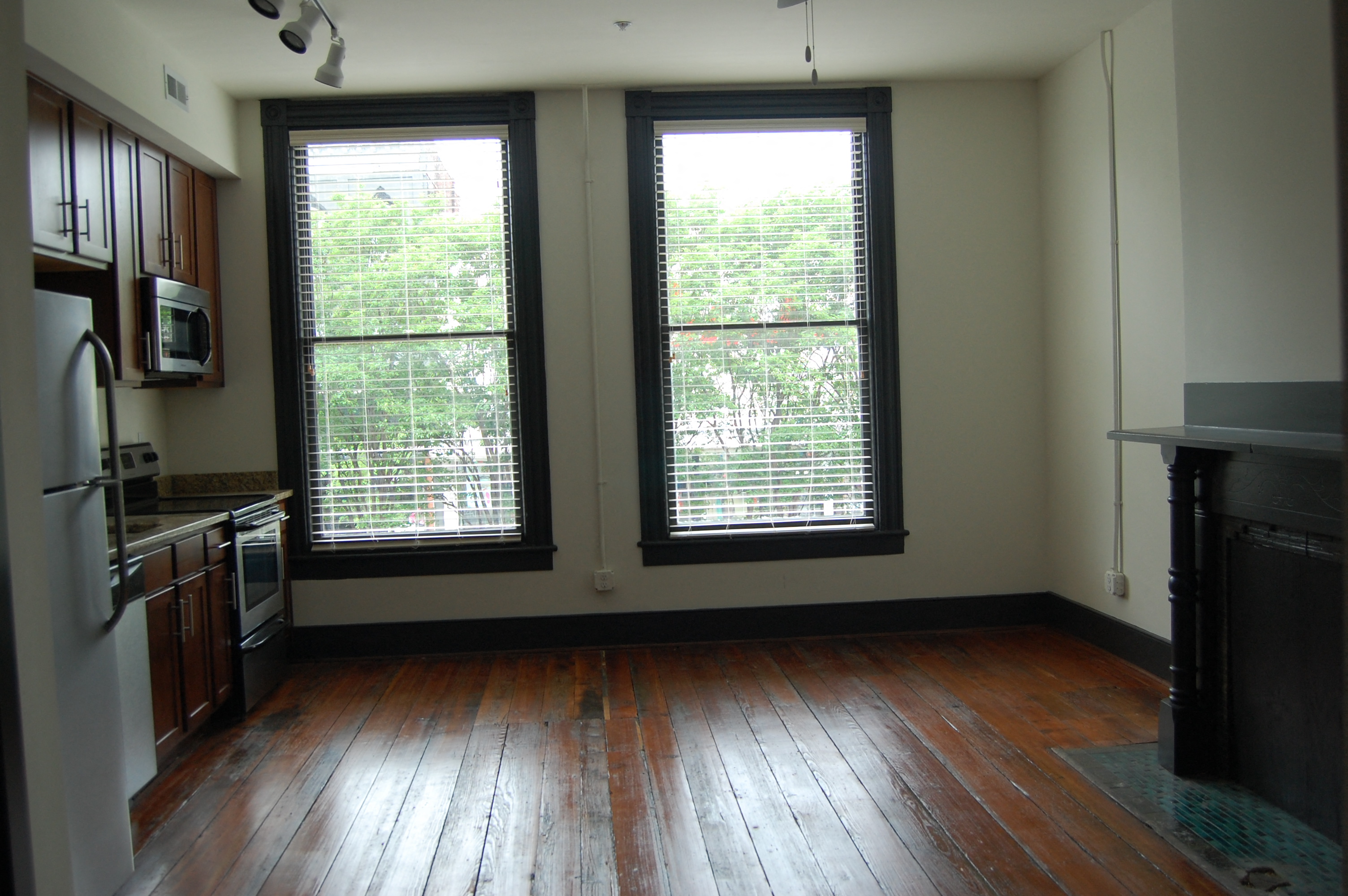 an empty kitchen with two large windows and wood floors