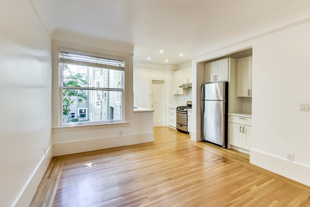 an empty living room with a large window and a kitchen