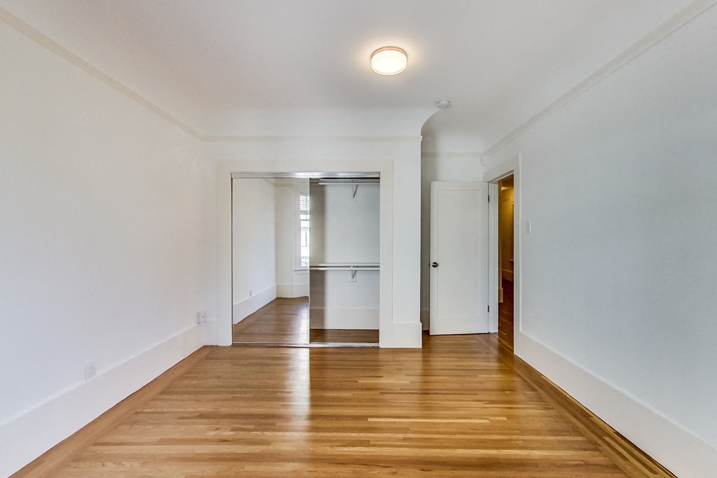 a living room with white walls and a wooden floor and a door to a kitchen