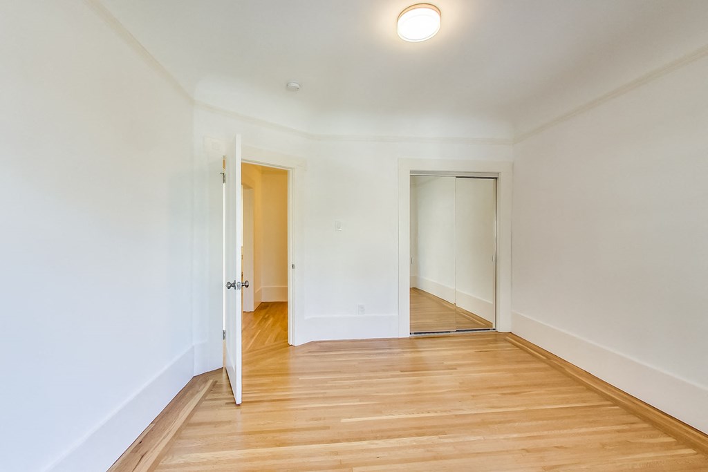 a living room with white walls and wood flooring and a door to a hallway