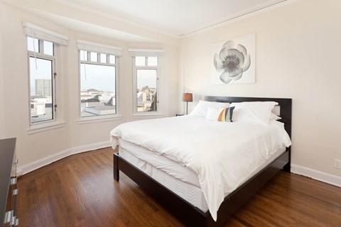 A bedroom with a large bed and a view of the city through the windows.