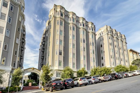 A row of parked cars in front of a large building with a gate.
