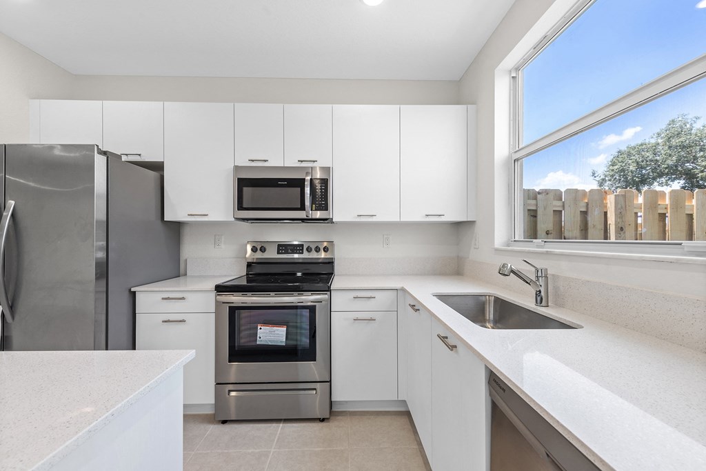 a white kitchen with stainless steel appliances and a window