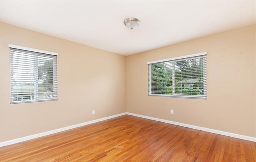 an empty room with a hard wood floor and two windows