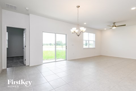 A spacious room with a sliding glass door leading to a balcony, a ceiling fan, and a chandelier.