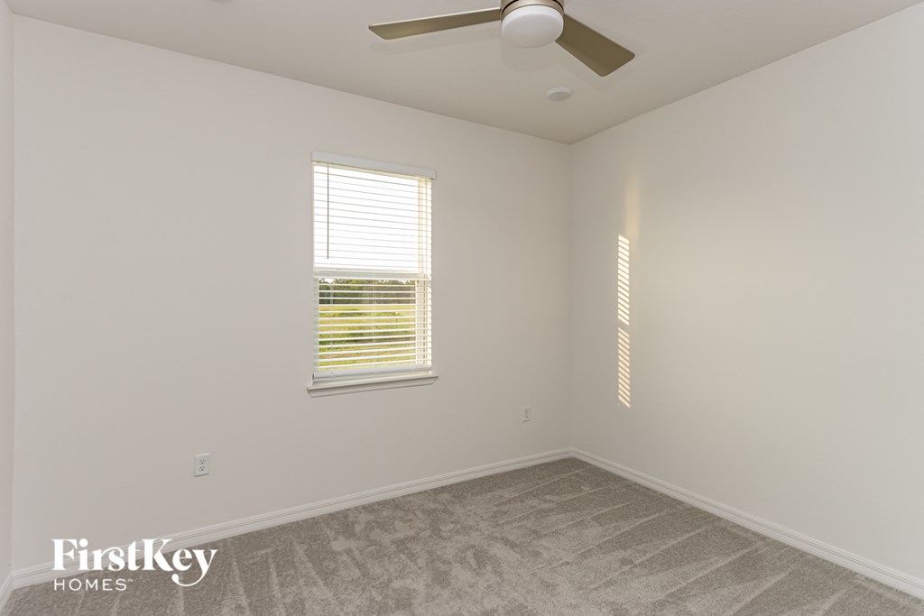A room with a fan, a window with blinds and a wall with a FirstKey Homes logo.